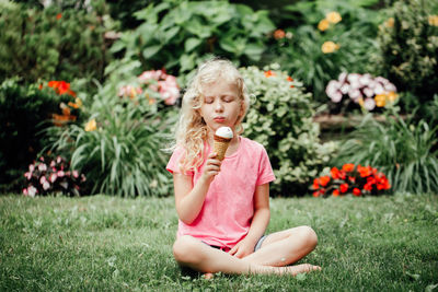 Cute funny girl sitting on grass in park eating licking ice cream from waffle cone. 