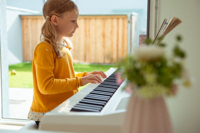 Side view of girl playing piano while siting at home