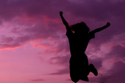 Low angle view of silhouette man with arms raised against sky during sunset