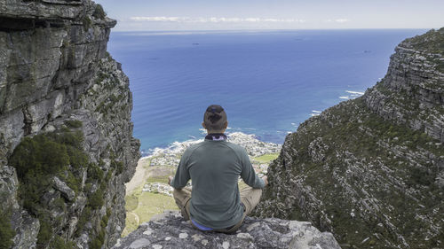 Rear view of man sitting on rock by sea