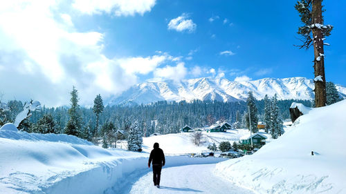 Rear view of man walking on snow covered landscape against sky