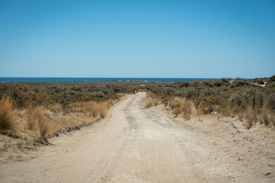 Dirt road amidst land against clear blue sky