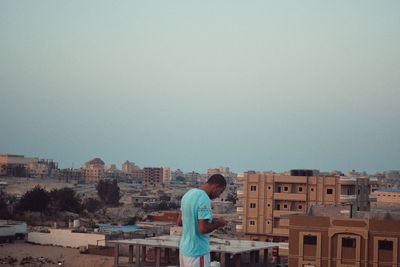 Young woman standing against buildings against clear sky