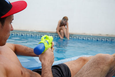 Man pointing squirt gun on woman sitting at poolside