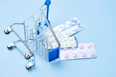 High angle view of pill spilling from shopping cart over blue background