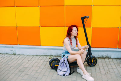 Woman uses a smartphone and an electric scooter in the summer in the city