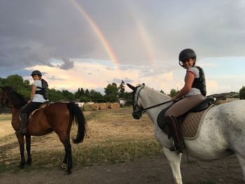 Girls riding horses against rainbow in sky