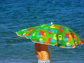 Midsection of shirtless man by parasol against sea