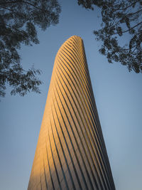 Low angle view of modern skyscraper against sky and framed with trees