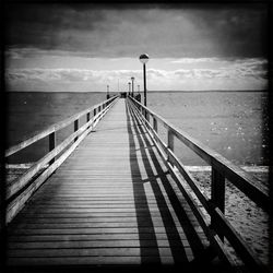 Pier on sea against cloudy sky