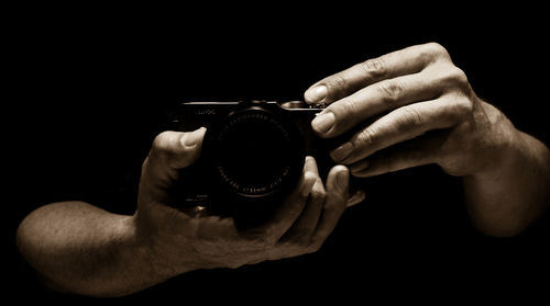 Cropped image of hands holding camera against black background