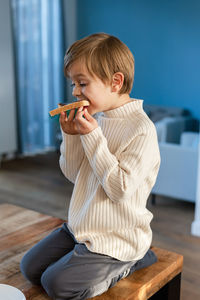 A boy bites into a sandwich with hazelnuts and cocoa, sitting on a table in the living room.