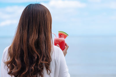 Rear view of woman holding watermelon at beach