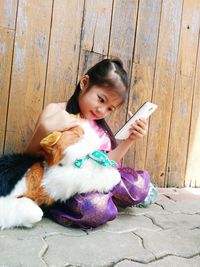 Cute girl holding smart phone while lying on wood