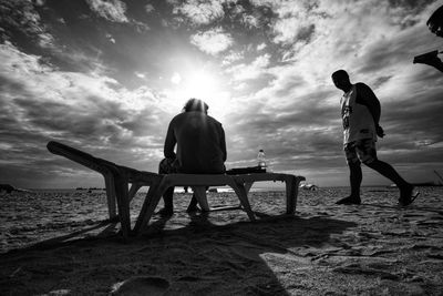 Rear view of men sitting on bench at beach