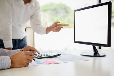 Cropped hands of man analyzing data by colleague gesturing towards computer