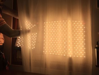 Low section of woman standing against illuminated curtain at night