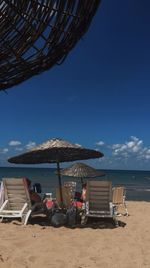 Lounge chairs and parasols on beach against blue sky