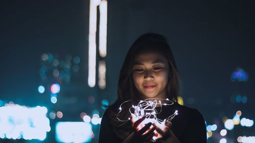 Portrait of woman holding illuminated lights at night