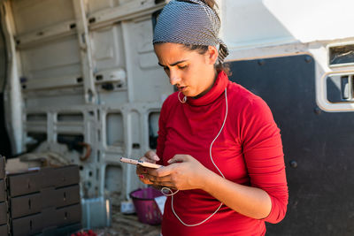 Concentrated female gardener in bandana browsing cellphone while working in farm and looking at screen