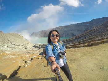 Woman wearing sunglasses standing on mountain against sky