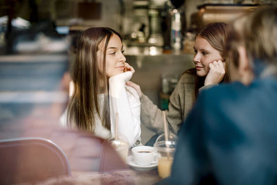 Teenage girl looking at friend while sitting in cafe