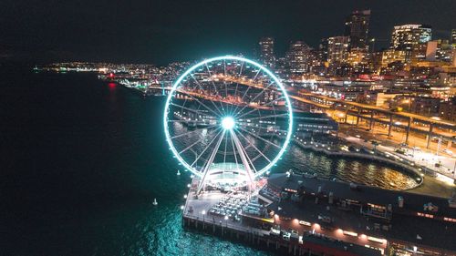 Aerial view of illuminated ferris wheel by river at night