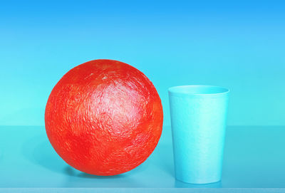 Red ball and plastic cup on the blue background - abstract geometric design with space for copy.