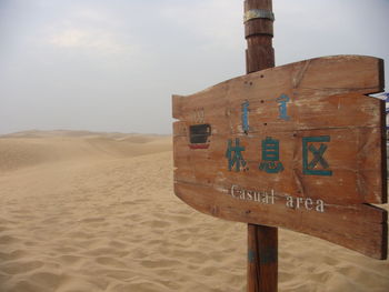 Information sign on sand at desert against sky