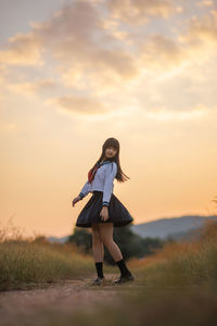 Rear view of woman standing on field against sky during sunset