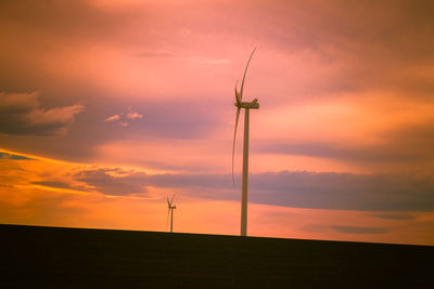 Silhouette wind turbines on field against sky during sunset