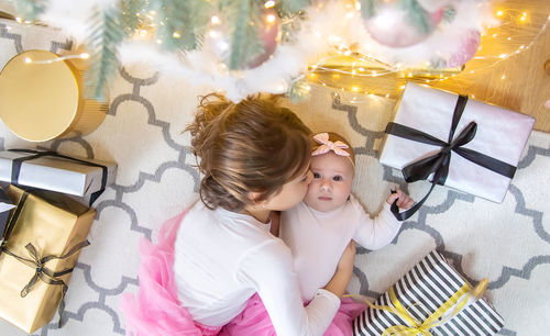 High angle view of girl kissing sister amidst gifts at home