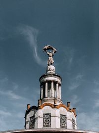 Low angle view of statue by building against sky, spire of a building built during the ussr.