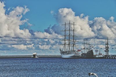 Seagulls flying over sea with sailing ships against sky