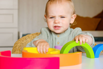 Little baby child in clothes made of natural fabric plays with rainbow colored wooden toys at table