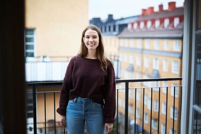 Portrait of smiling young woman standing against railing