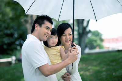 Happy family with white umbrella looking away at park