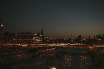 Illuminated bridge over river by buildings against sky at night