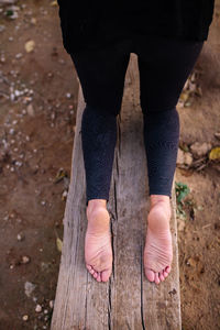 Low section of woman kneeling on wooden plank outdoors