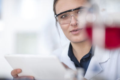 Scientist working in lab holding a tablet looking at flask