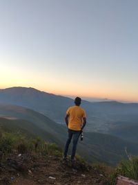 Rear view of man standing on mountain against sky