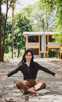 Portrait of smiling young woman throwing leaves while sitting on road in forest