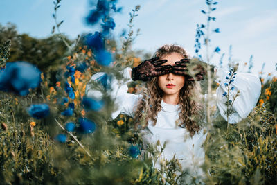 Beautiful young woman  with lace gloves standing in wild flowers in summer