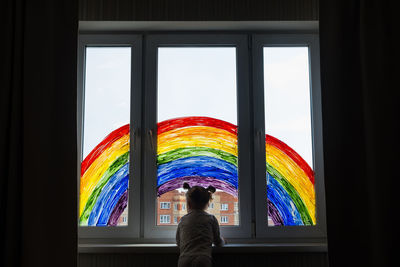 Little girl on background of painting rainbow on window. kids leisure at home. 