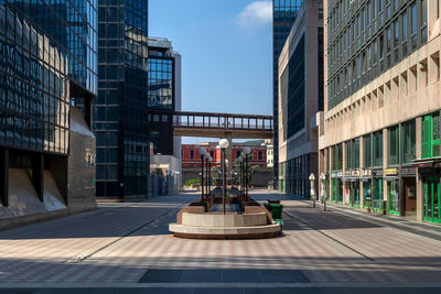 Courtyard with marble benches and lampposts between modern buildings with mirrored facades.