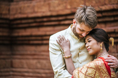 Couple embracing while standing against building