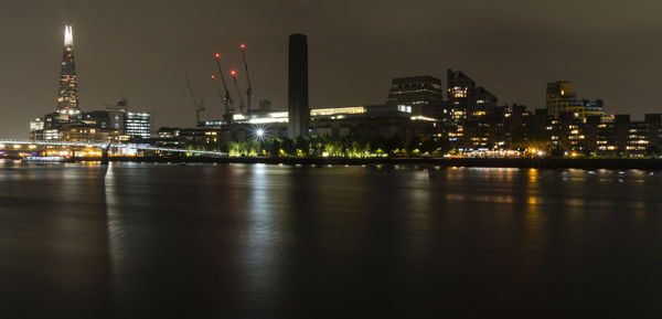 Illuminated buildings by river against sky at night