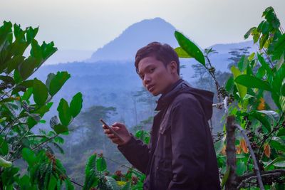 Young man using smart phone while standing on mountain