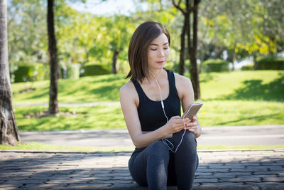 Young woman using mobile phone while sitting on tree