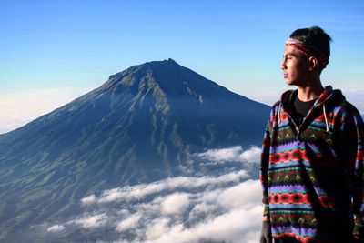Young man looking at mountains against clear blue sky